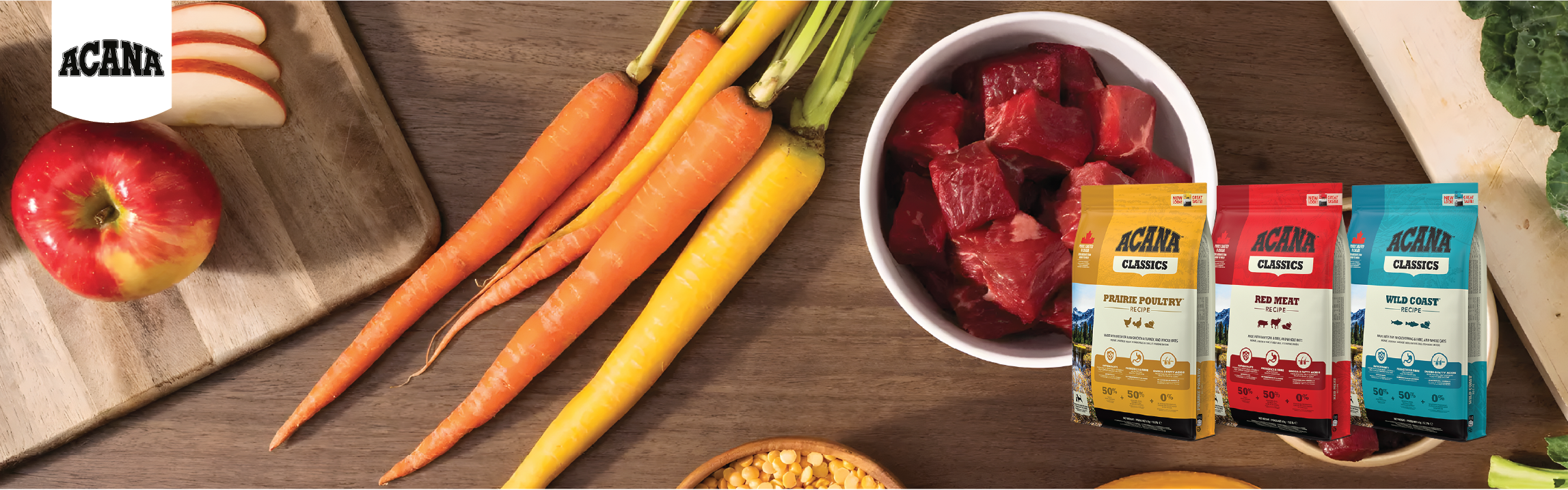 Assorted Acana pet food packages with raw meat, carrots, apples, and a cutting board on a wooden surface.